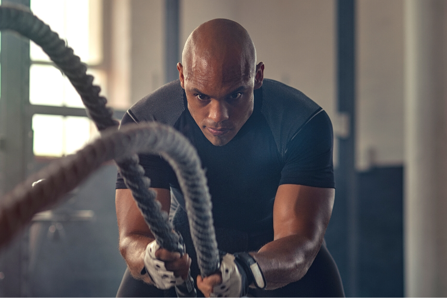 Vista lateral del adulto joven seguros crossfit hombre con cabello rizado  de larga data y hacer ejercicios en el gimnasio trx solos, capacitación,  entrenamiento de pecho en el rin Fotografía de stock 